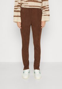 Brune suedebukser med en slim fit, som har en glatt tekstur og subtile folder. Kombinert med hvite joggesko med grønne detaljer.