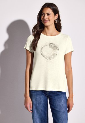 Light yellow short-sleeve t-shirt featuring a circular graphic with lines radiating outward, paired with blue jeans. Soft fabric texture.