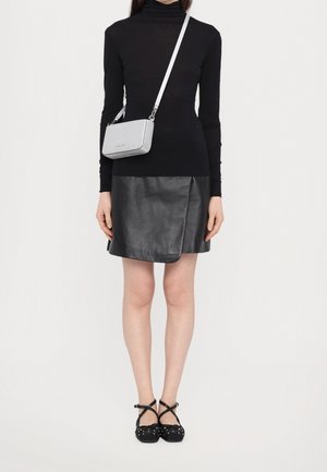 Vrouw met een zwarte coltrui, een zwarte leren rok, zwarte platte schoenen met studs en een klein zilveren crossbodytasje.