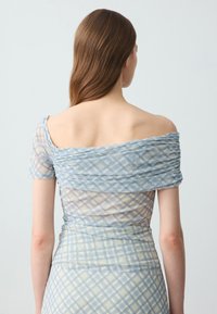 Abito arricciato in tessuto leggero con design a spalle scoperte, caratterizzato da una fantasia a quadri blu e beige. Texture morbida e silhouette aderente.