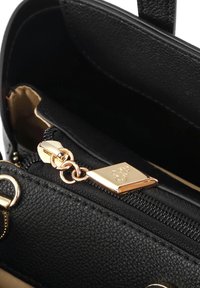Interno di una borsa a tracolla in pelle nera texturizzata con una zip dorata e un accento metallico. Presenta un logo dorato e un colore interno a contrasto.