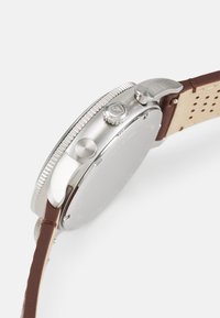 Silberner Edelstahl-Uhr mit einem polierten Rahmen, braunem Lederarmband und strukturierter Krone. Verfügt über einen glatten, minimalistischen Gehäuseboden.
