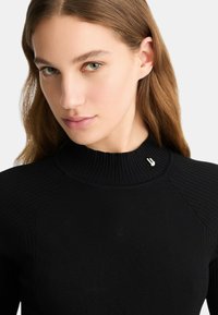 Maglione a collo alto nero con costine, caratterizzato da un alto collo e dettagli in metallo argentato, design aderente con una leggera texture.