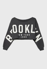 Sweatshirt noir court avec un grand texte blanc "BROOKLYN" sur le devant et les manches, et "New York 1986" imprimé sous le texte principal.