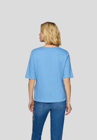 Helles blaues, strukturiertes Kurzarmoberteil mit einem quadratischen Ausschnitt, kombiniert mit eng anliegenden Jeans aus Denim mit tonalem Stich und Gesäßtaschen.