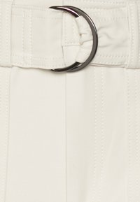 Cinto branco feito de tecido com uma textura suave, apresentando uma elegante fivela circular preta e detalhes plissados na faixa.