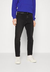 Zwarte denim jeans met een slimfit, vijf-pocket ontwerp en zilveren hardware, gecombineerd met witte sneakers en een blauwe hoodie.