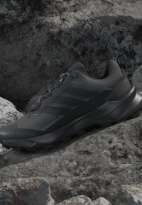 Basket de sport noire avec semelle texturée et languette reposant sur des rochers gris irréguliers.