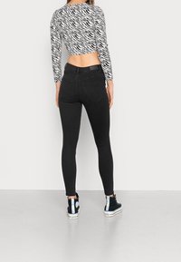 Jeans ajustados negros de cintura alta con dos bolsillos traseros, combinados con un top corto de estampado de cebra en blanco y negro y zapatillas con toques azules.