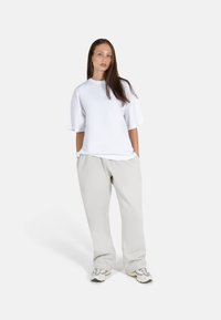 Hvit oversized t-skjorte med korte ermer, sammen med lysegrå joggebukser. Antrekket har en avslappet passform og jevn tekstur.