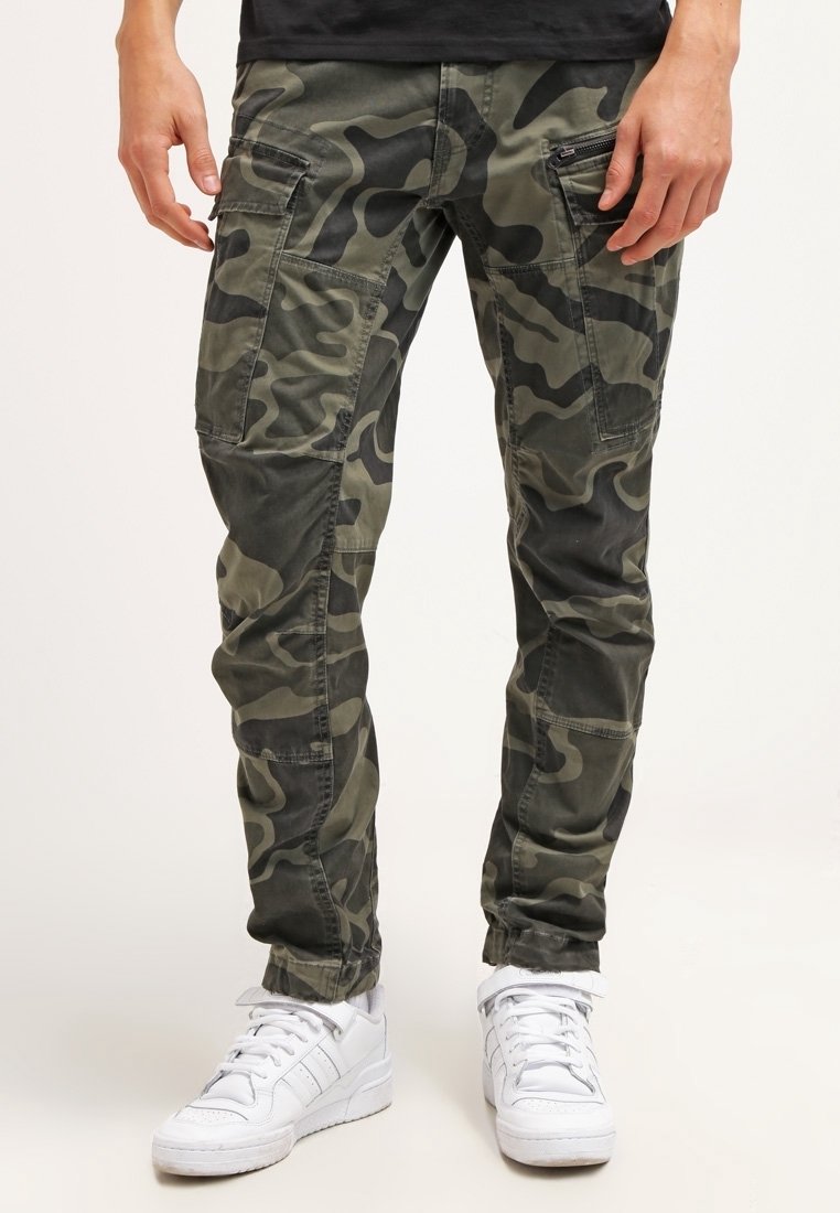 Pantalons cargo camouflage en vert olive avec un motif texturé, dotés de plusieurs poches et d'une coupe slim, associés à des baskets blanches.