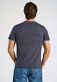 Mörkgrå t-shirt med kort ärm och rund halsringning samt en slät textur. Kombinerad med blå denimjeans som har två bakfickor.