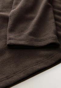 Brown ribbed fabric with a soft texture, featuring a folded sleeve and stitched hem. The design is simple and functional.