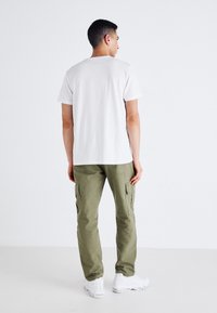 Fehér pamut póló olíva zöld katonai nadrággal, amely oldalzsebekkel és elasztikus szegélyekkel rendelkezik, fehér sportcipővel viselve.