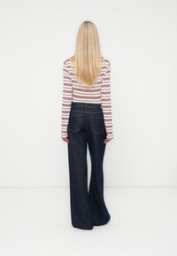 Haut à manches longues rayé avec des rayures rouges et blanches, associé à un jean en denim noir à jambes larges. Texture lisse et design classique.