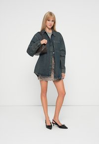Džínová oversized košeľa, svetlomodrá, s gombíkmi, detail vrecka; nosená cez leopardí potlač mini sukňu; skombinovaná s čiernymi sandálmi na podpätku a hnedou kabelkou.