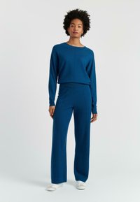 Blauer Strickpullover und passende weit geschnittene Hose, mit gerippter Textur und Nähten, kombiniert mit weißen Sneakers.