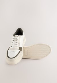 Sneakers med hvidt læderoverflade og olivengrønne ruskindsdetaljer, rund snude, flade snørebånd og tekstureret cremefarvet gummisål.