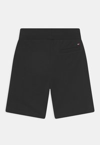 Pantaloni corti neri casual con vita a coste, tasca posteriore a filetto e piccolo logo rosso, bianco e blu vicino alla tasca su uno sfondo semplice.