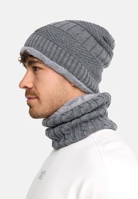 Bonnet gris tricoté avec un design côtelé et une doublure en fausse fourrure, accompagné d'un cache-cou gris assorti avec un motif en torsades tricotées.