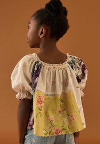 Blusa a fantasia floreale con maniche a sbuffo, caratterizzata da una sezione con pizzo giallo sul retro, realizzata in tessuto leggero.
