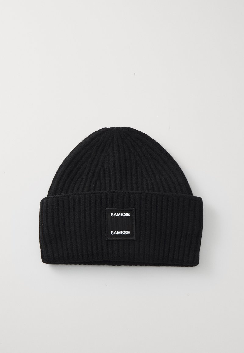 Cappello beanie nero a coste con risvolto. Presenta due etichette nere rettangolari con testo bianco. Materiale in maglia morbida, forma ovale nella parte superiore.