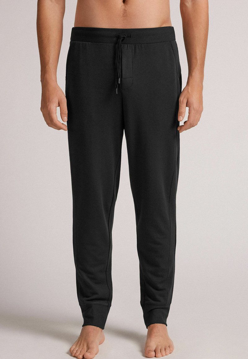Zwarte jogginsbroek van zachte stof, met een elastische tailleband met een trekkoord, zijzakken en geribbelde boorden bij de enkels.