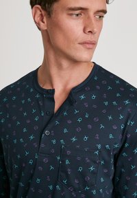 Marineblauseshirt mit langen Ärmeln und Rundhalsausschnitt, das mit einem Muster aus bunten astrologischen Symbolen verziert ist. Enthält eine Brusttasche und Knöpfe.