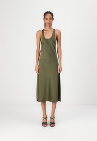 Rochie din satin verde măslin, cu decolteu în formă de cerc, croială ajustată și fente laterale. Asortată cu sandale negre cu toc înalt și bretele.