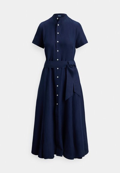 Haljina od lanene tkanine tamnoplave boje s mandarinskim ovratnikom, kratkim rukavima, kopčanjem sprijeda na gumbe i pojasom u struku. Ima lepršavu suknju.