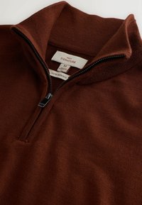 Tamsiai ruda merino vilnos zip-up palaidinė. Turi stovinčią apykaklę, pusiau užtrauktuką ir lygų paviršių su subtiliomis siuvimo detalėmis.
