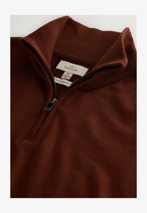 Rozpinana bluza z wełny merino w głębokim brązie. Posiada stójkę, zamek na pół długości oraz gładką fakturę z subtelnymi detalami ściegów.