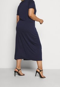 Navy blue, knee-length, short-sleeve dress made of soft fabric. Features a relaxed fit and a slightly curved hem. Paired with black high-heeled sandals.