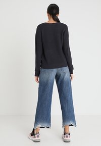 Pull en tricot bleu marine à texture côtelée, associé à un jean en denim délavé à jambes larges avec des bords effilochés. Le modèle porte des baskets à accents roses.
