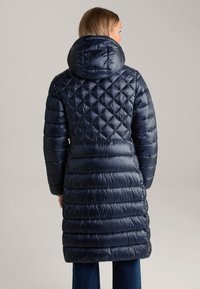 Lange marineblauwe pufferjas met een capuchon, voorzien van diamant- en horizontale quiltpatronen, glanzende textuur en elastische manchetten.