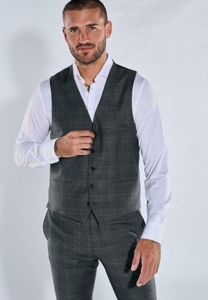 Grauer, karierten Weste mit taillierter Passform, getragen über einem weißen Hemd. Verfügt über eine Fronttasche und vier Knöpfe zum Schließen. Glatte Textur.