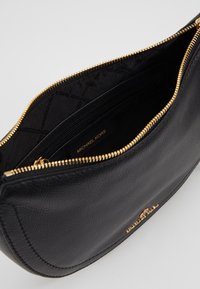 Bolso de piel negra con un acabado texturizado, cremallera dorada y herrajes. El interior presenta un logo y un pequeño bolsillo con cremallera.