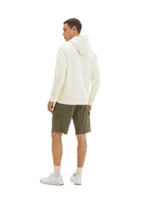 Cremefarvet hoodie med en front-overskæring, parret med olivengrønne cargo shorts og hvide sneakers, set fra ryggen.