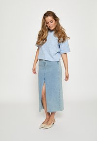 Gaiši zils adīts īsais tops, kas saskaņots ar gaiši zilu džinsu svārku ar priekšējo izgriezumu. Valkāts ar bēšām šaurām kurpēm.