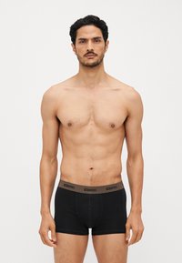 Schwarze Baumwoll-Boxershorts mit einem markierten Bund. Der Stoff ist glatt; das Design weist einen figurnahen Schnitt und flache Nähte für einen hohen Tragekomfort auf.