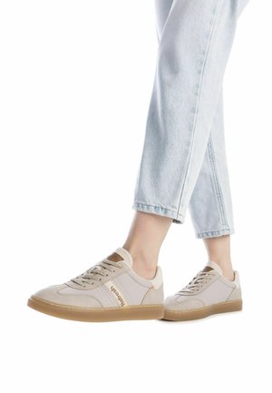 Zapatillas beige claro con una textura suave, con suela de goma, diseño de cordones y acentos en contraste. Combinadas con jeans azul claro.