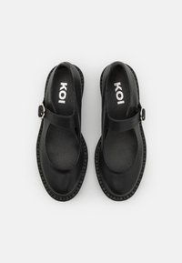 Black Mary Jane shoes with a rounded toe, featuring a strap with a silver buckle, and textured rubber sole. Soft leather upper and interior.