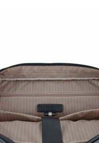 Graue Reisetasche mit Innenfutter im Fischgrätmuster in Beige. Enthält ein schwarzes Etikett und eine horizontale Reißverschlusstasche zur Organisation.