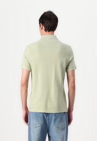 Polo em tecido verde claro, mangas curtas, colarinho clássico e um corte relaxado. Combinado com jeans azul claro, exibido pela parte de trás.