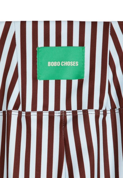 Tissu rayé vertical marron et blanc avec une étiquette verte cousue portant la mention "BOBO CHOSES" en lettres beiges.