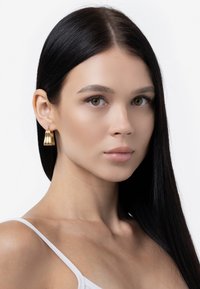 Kultatiput, joissa on viistetty muotoilu, roikkuvat korvalehdestä. Ne ovat kiiltäviä ja sileäpintaisia.