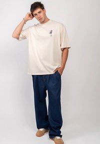 Beige lyhythihainen t-paita, jossa pieni sininen kuvio. Yhdistetty löysiin sinisiin farkkuihin ja vaaleanruskeisiin tennareihin. Yksinkertainen, rento istuvuus.