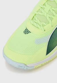 Baskets de sport néon vert vif avec tige en mesh, superpositions texturées et semelle extérieure bleu clair. Lacets et accents assortis en vert.