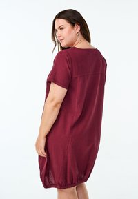 Burgundy kortärmad klänning med avslappnad passform, rundad halsringning och elastisk nederkant vid midjan, tillverkad av lättviktsmaterial.