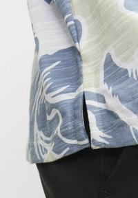 Kortärmad skjorta med ett blått och vitt blommönster, tillverkad av lättviktsmaterial med en avslappnad passform och sidslits.